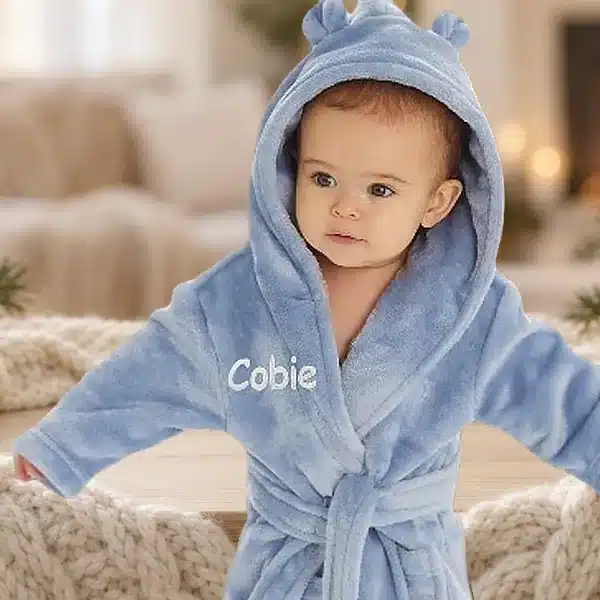 Baby in a blue personalised hooded robe embroidered with Cobie