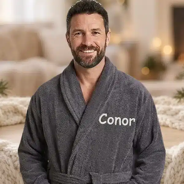 Man in a dark grey personalised towelling robe embroidered with Conor