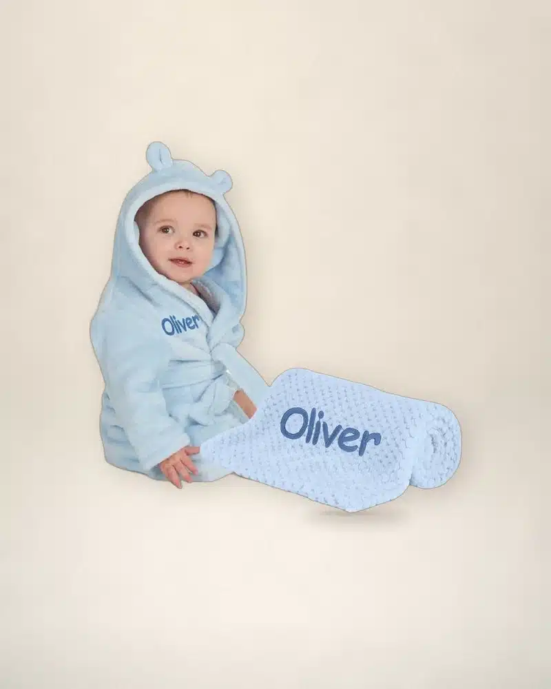 Baby in a blue personalised robe with a matching blanket, both embroidered with Oliver