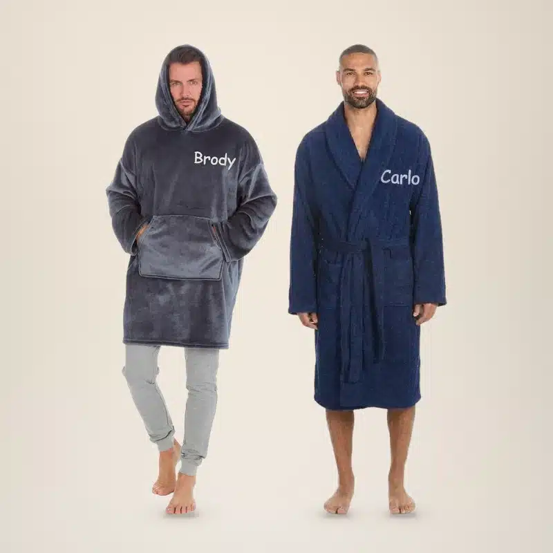 Man in a charcoal personalised oversized hoodie embroidered Brody next to a man in a navy towelling robe embroidered Carlo