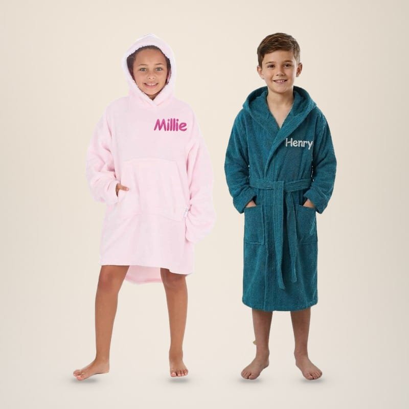 Girl in a pink personalised kids hoodie embroidered Millie next to a boy in a teal kids towelling robe embroidered Henry