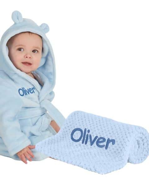 Baby in a blue personalised robe with a matching blanket, both embroidered with Oliver